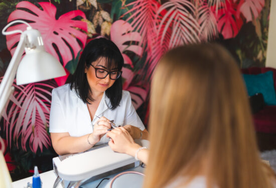 A young beautician is working with a client in a salon. She is doing manicure.