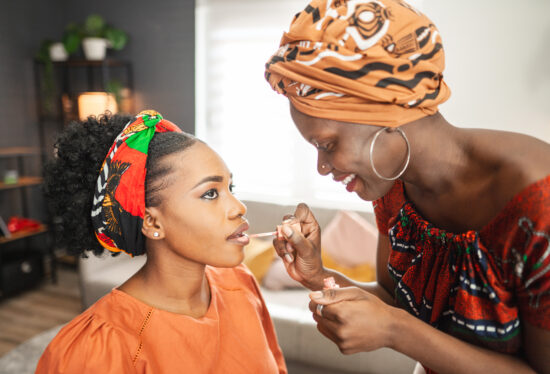 Black make up artist applying lipstick on lovely black woman